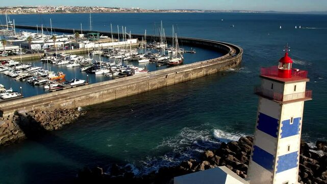 Aerial drone pull back from Santa Marta Lighthouse in Cascais, Portugal. Scenic view of coastal museum, marina and Atlantic ocean waves hitting cliffs. Beautiful travel destination, 4k video.