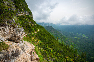 Mountain trail in the Dolomites (Dolomiti, Dolomiten), Italy, leading to Lago Sorapis. The path winds along rocky slopes with stunning views of valleys, forests, and peaks