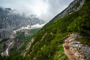 Mountain trail in the Dolomites (Dolomiti, Dolomiten), Italy, leading to Lago Sorapis. The path winds along rocky slopes with stunning views of valleys, forests, and peaks