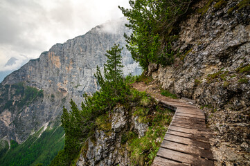 Mountain trail in the Dolomites (Dolomiti, Dolomiten), Italy, leading to Lago Sorapis. The path winds along rocky slopes with stunning views of valleys, forests, and peaks