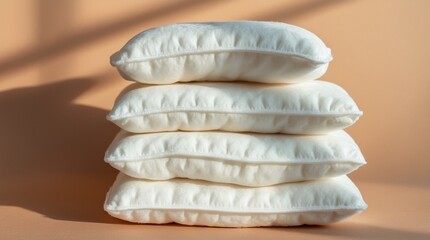 Neatly stacked white pillows on a beige background in soft natural lighting.  
