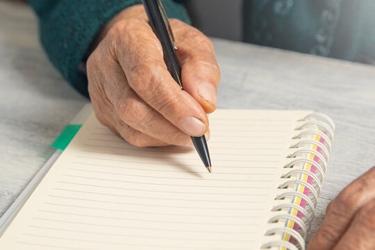 Caucasian elderly woman writes in notepad.
