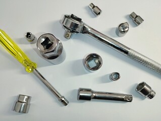 On a white background, scattered school tools, namely a screwdriver and a wrench with interchangeable nozzles of different sizes.