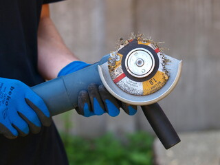 Worker Holding a Damaged Angle Grinder: Worn Cutting Disc with Embedded Metal Wires in Protective...