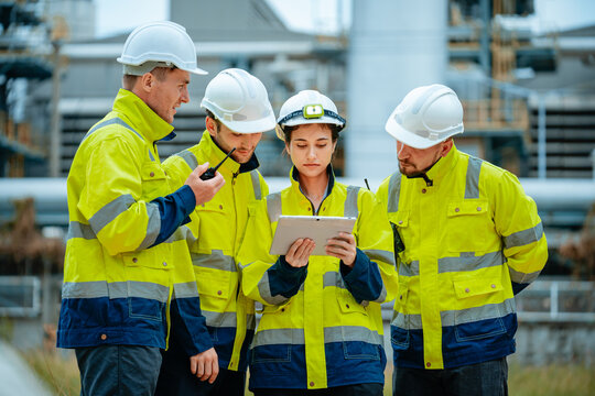 Construction team discusses project details at industrial site during daytime with safety gear and technology