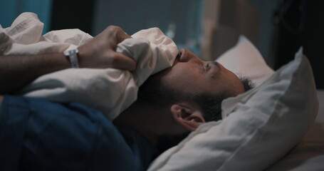 Man in hospital bed, then moves to couch, covers with blanket he's not feeling good.