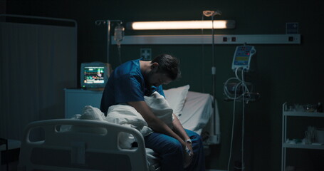 Exhausted ill male patient in hospital ward sits on bed then leaves.