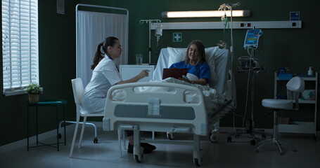 Obraz premium Doctor seated beside elderly patient, providing document for her to sign.