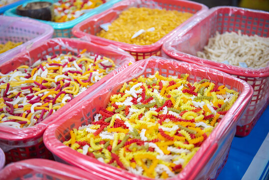 Colorful macaroni, pasta, helical corkscrew fusilli, vegetable flat noodles in large plastic basket with clear liner and desiccant bag at local market in Can Tho, Vietnam, organic raw ingredient