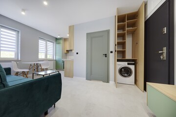 Salon w nowoczesnym apartamencie z seledynowym aneksem kuchennym z ciemnozieloną sofą © arteffect.pl