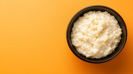 Creamy Pale Yellow Food in Dark Brown Bowl Against Vibrant Orange Background