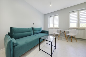 Salon w nowoczesnym apartamencie z seledynowym aneksem kuchennym z ciemnozieloną sofą © arteffect.pl