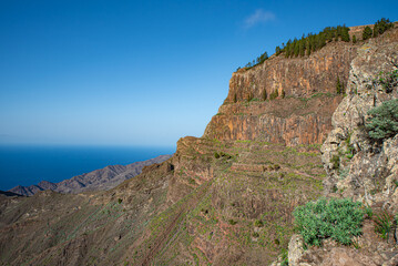 Rocky cliffs and mountains seen from a hiking trail near the village Arure. Barranco de Taguluche canyon and the Atlantic Ocean. La Gomera, Canary Islands, Spain