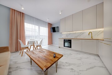 Salon w nowoczesnym apartamencie z beżowym  aneksem kuchennym z rudą jasno brązową pluszową sofą © arteffect.pl