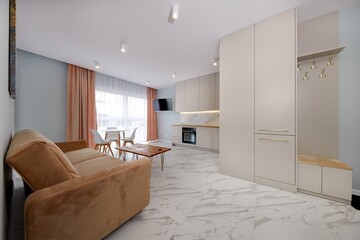 Salon w nowoczesnym apartamencie z beżowym  aneksem kuchennym z rudą jasno brązową pluszową sofą © arteffect.pl