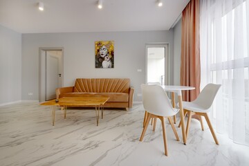 Salon w nowoczesnym apartamencie z beżowym  aneksem kuchennym z rudą jasno brązową pluszową sofą