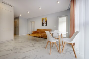 Salon w nowoczesnym apartamencie z beżowym  aneksem kuchennym z rudą jasno brązową pluszową sofą