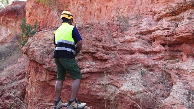 The geologist is carefully examining the reddish rock formation in the field.