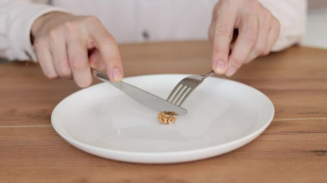 A man who is eating only one walnut on a empty plate. Dieting concept.