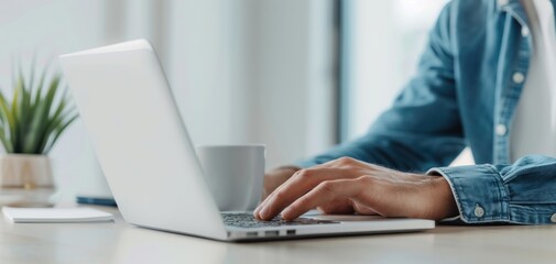 Person typing on a laptop with a coffee cup and a plant nearby.