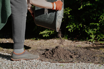 Partially visible woman pouring soil out of a big black bucket