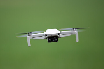 Front view of a flying drone with a camera. Flying small consumer quadcopter on background of green field
