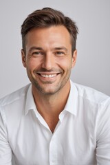 smiling man in white shirt sitting down and looking at camera