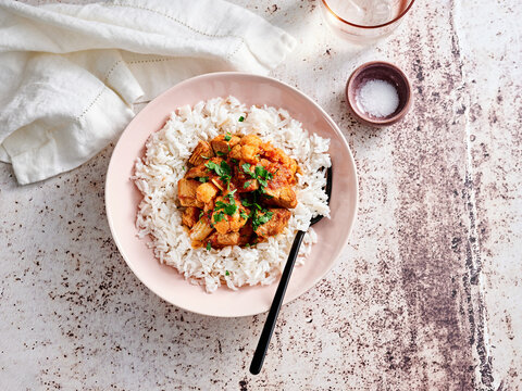 Tender chicken pieces simmer with aromatic spices, served over a bed of fluffy white rice. Fresh herbs garnish the dish, adding a pop of color and flavor