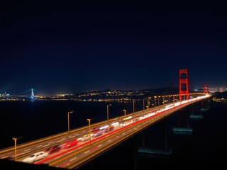 Fototapeta premium Long shot of the Richmond-San Rafael Bridge illuminated at night with blurred traffic and distant city lights, California coastline, highway photography