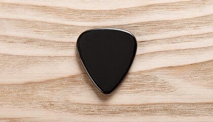 Plastic black guitar pick isolated on wooden background. Music concept. Flat lay. Mock-up.