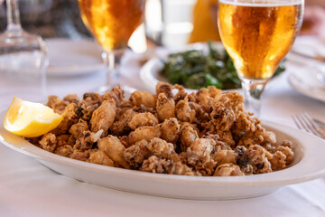 Traditional Mediterranean fried calamari (chipirones) golden and crispy, presented with a lemon wedge and paired with drinks and greens in a casual dining setup