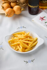 Warm Toned Still Life of Golden French Fries in Rustic White Bowl on Embroidered Tablecloth