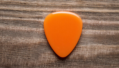 Plastic orange guitar pick isolated on wooden background. Music concept. Flat lay. Mock-up.