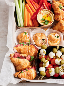 A vibrant spread of appetizers includes flaky croissants filled with savory meat, colorful vegetables, tasty dip, and delightful cheese skewers, perfect for casual events
