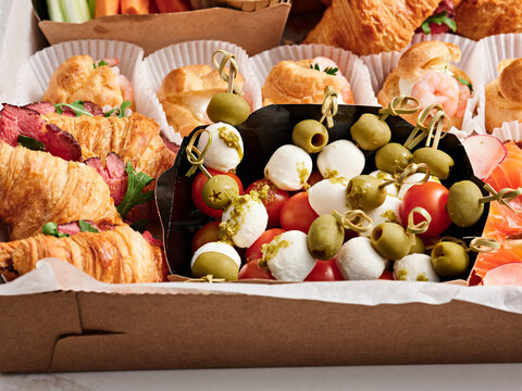 A diverse platter features fresh croissants, savory rolls, and bite-sized skewers with tomatoes, mozzarella, and olives. Perfect for a light lunch or snack at a friendly gathering