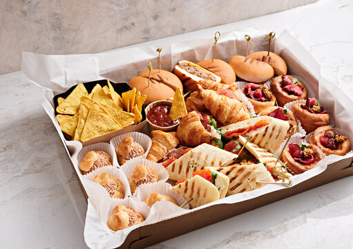 A variety of snacks and pastries are beautifully arranged in a large tray. There are sandwiches, rolls, chips, and sweet treats, perfect for a social event