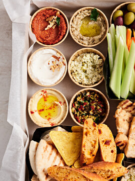 A colorful platter displays various dips like hummus, baba ganoush, and tzatziki alongside fresh vegetable sticks and warm pita bread, perfect for sharing at a lively gathering