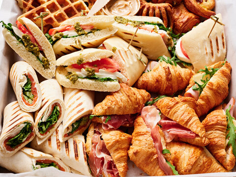 A variety of sandwiches, croissants, and pastries are beautifully arranged for a brunch. Fresh ingredients include greens and rich spreads, appealing to all tastes