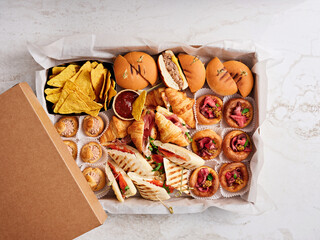A colorful spread of assorted appetizers is arranged on a light surface, featuring sliders, nachos, and dips, ideal for sharing during a social gathering