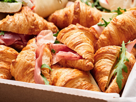 A tray filled with golden-brown croissants stuffed with slices of ham and fresh arugula, perfect for a breakfast or brunch occasion, inviting and delicious
