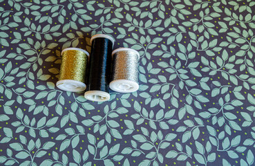 Reels of metalic thread, gold, silver and black on a green floral background
