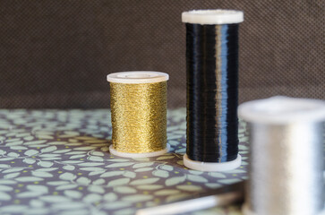 Reels of metalic thread, gold, silver and black on a green floral background with scissors