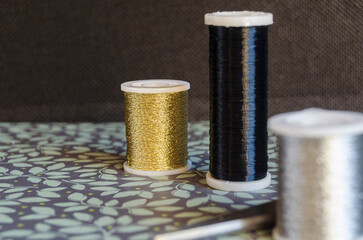 Reels of metalic thread, gold, silver and black on a green floral background with scissors