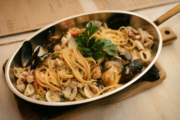 Hot plate of delicious spaghetti with mussel, clam, shrimps and squid on wooden cutting board