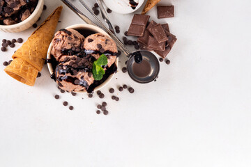 Double chocolate ice cream bowl with ice cream waffle cones on white table background. Homemade chocolate gelato with dark chocolate drops and chocolate topping sauce, sweet and tasty summer dessert