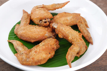 Fried chicken wings in a ceramic dish with banana leaves on a wooden table. Thai food.