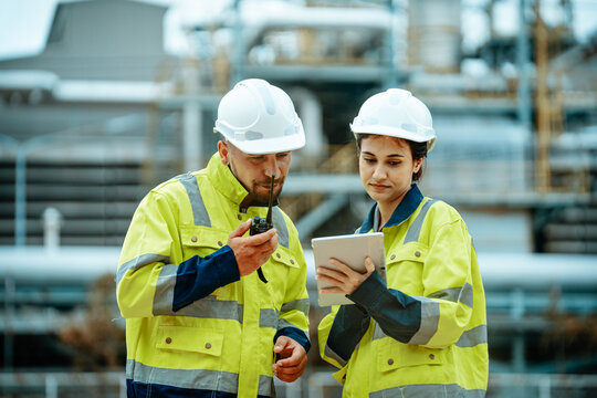 Workers collaborating at industrial site with communication device and tablet during project review