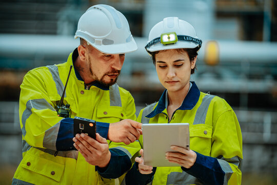 Workers in safety gear collaborate on a tablet in an industrial setting during the day, discussing project details and instructions