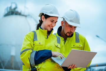 Workers collaborate on a project while using a laptop at an industrial site during the day