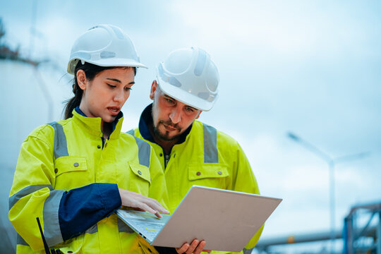 Engineers collaborate at a construction site while reviewing plans on a laptop in bright yellow safety gear
